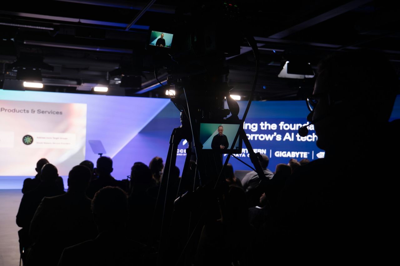 Camera operator on the stage during a keynote — viewfinder framing the speaker.